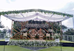 Tenda bening dengan dekorasi kain putih dan lampu gantung untuk pelaminan rooftop